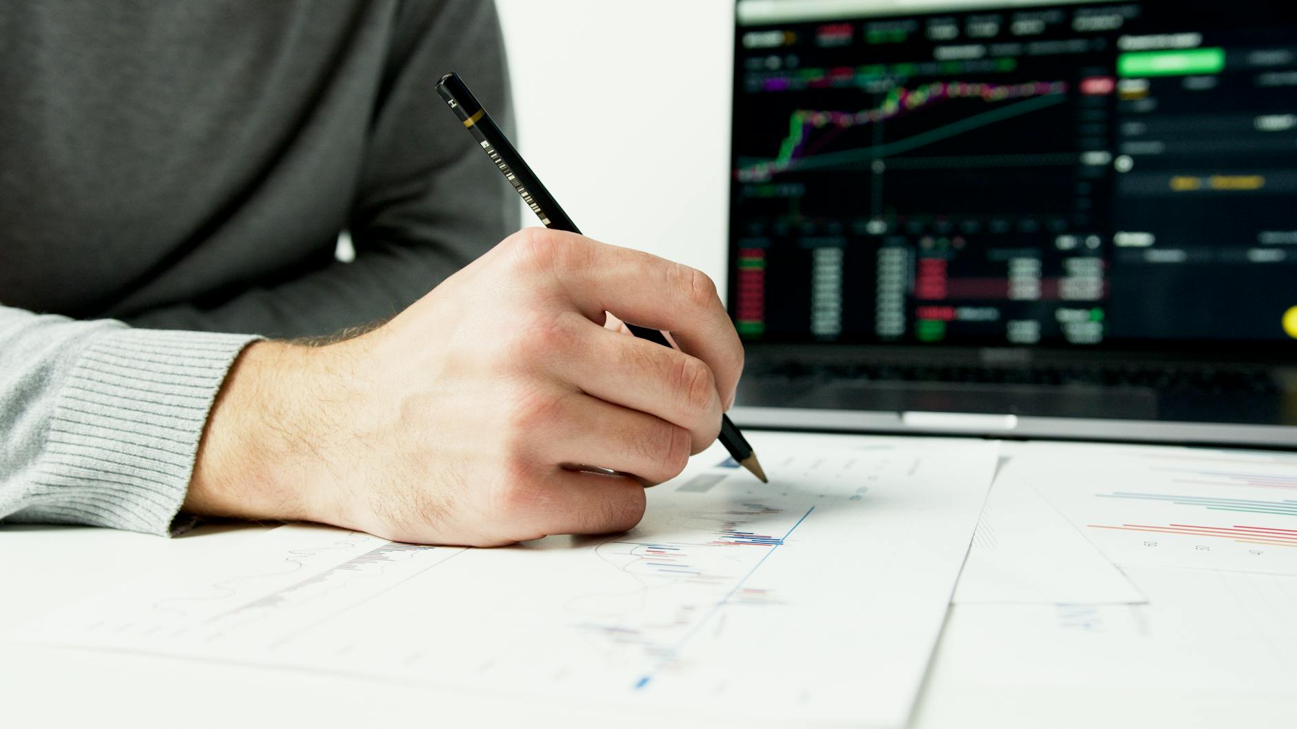 Ilustrasi: Close-up of a person analyzing financial charts with a laptop displaying stock market data.