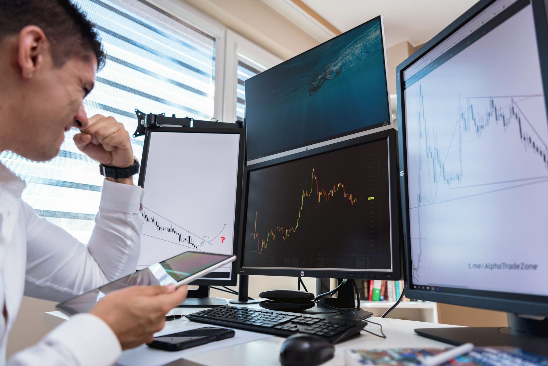 Ilustrasi: Trader in white shirt analyzing stock charts on multiple monitors during daytime in an office setting.