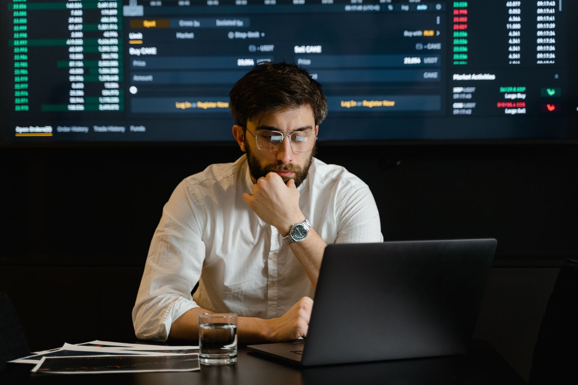 Ilustrasi: A man intensely analyzing stock market data on a laptop in an office setting.