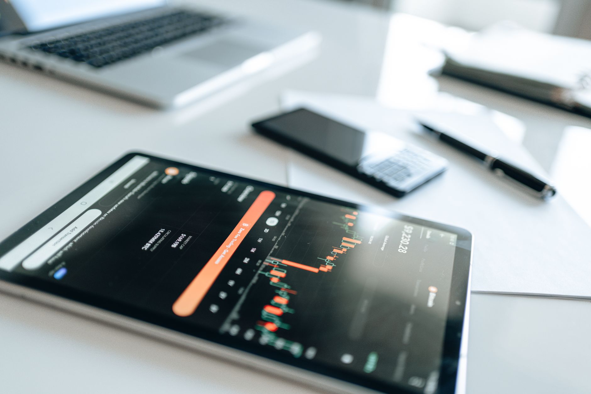 Ilustrasi: Modern financial tools including tablet with market trends on white desk setup.